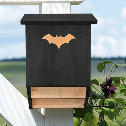 Outdoor wooden bat house mounted on fence post in garden - black cedar bat box to attract bats for insect control